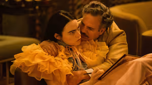 Bella Baxter (Emma Stone) embraced by Duncan Wedderburn (Mark Ruffalo) on sofa