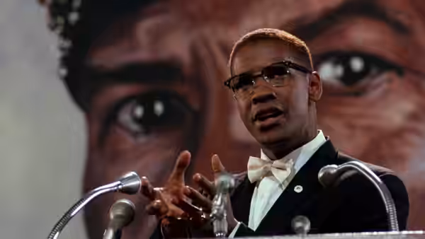 Malcolm X (Denzel Washington) gesturing while speaking at a podium