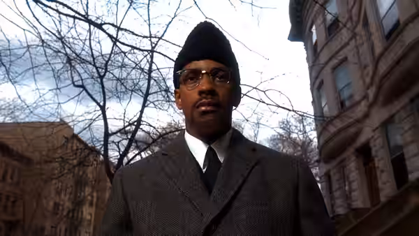 Malcolm X (Denzel Washington) standing on a city street in winter attire