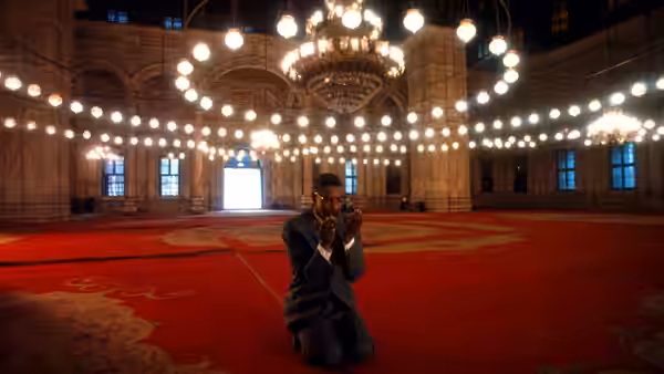 Malcolm X (Denzel Washington) kneeling in prayer inside a large ornate hall