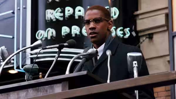Malcolm X (Denzel Washington) speaking at a podium with multiple microphones