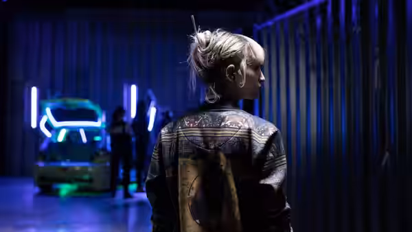 Alexia (Agathe Rousselle) looks toward a neon-lit car inside a garage