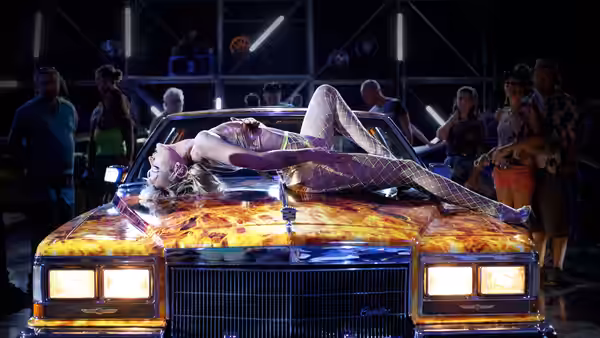 Alexia (Agathe Rousselle) lies across a customized car as onlookers gather