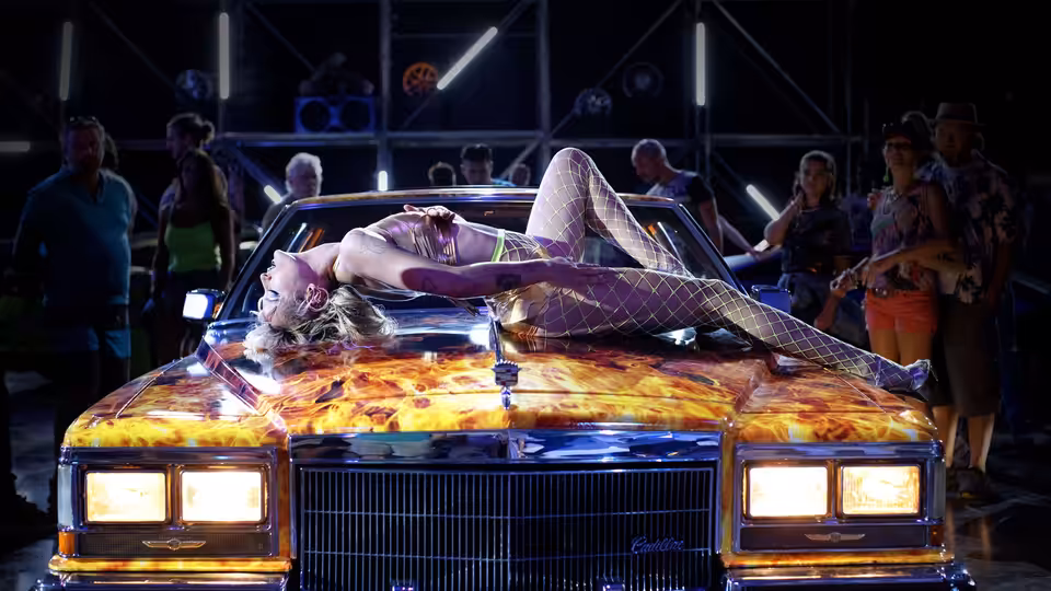 Alexia (Agathe Rousselle) lies across a customized car as onlookers gather