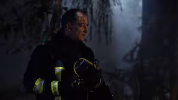 Vincent (Vincent Lindon), dressed as a firefighter, holds his helmet in a forest