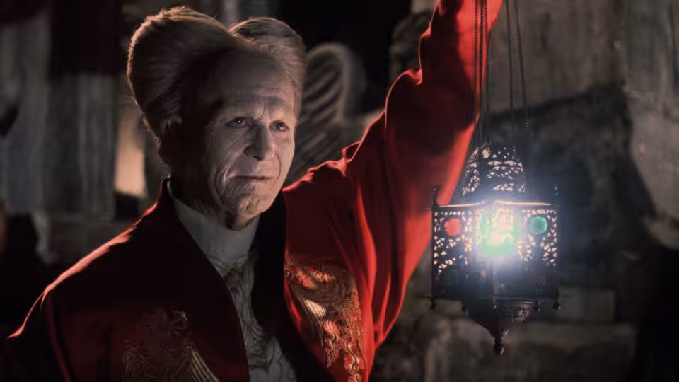 An older man in a red robe holds up a glowing lantern in darkness