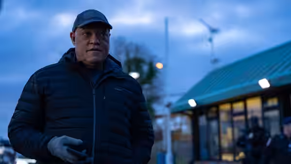 Director Moore (Holt McCallany) stands outside a modern glass-fronted building