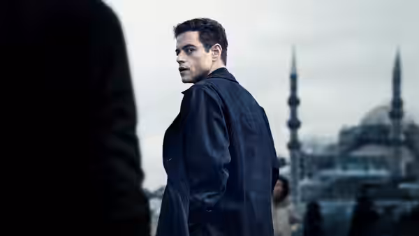 Heller (Rami Malek) looks back toward someone on a street lined with mosque minarets