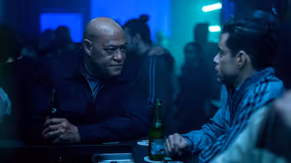 Henderson (Laurence Fishburne) talks with Heller (Rami Malek) at a dimly lit bar