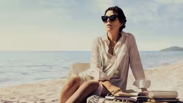 Leda Caruso (Olivia Colman) sits beside her books on the beach, looking out to sea