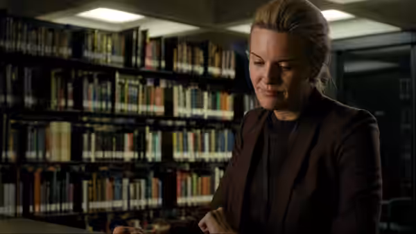 Amelia Pembrock (Maggie Grace) stands among library shelves