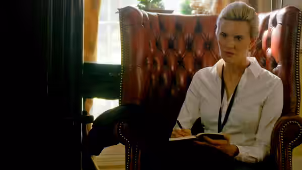 Amelia Pembrock (Maggie Grace) writes in a notebook from a leather armchair