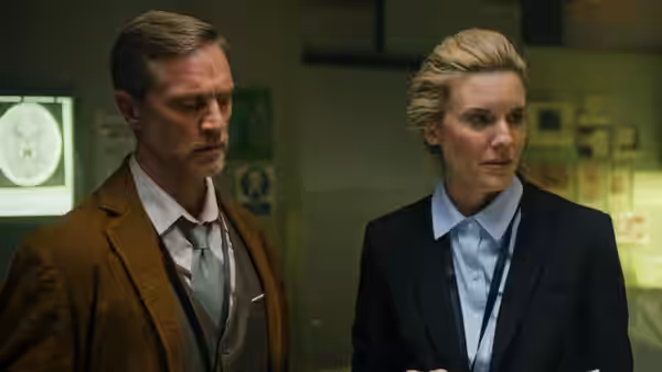 Amelia Pembrock (Maggie Grace) stands beside a man in a medical examination room