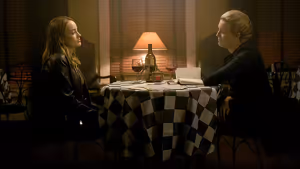 Two women sit across a table in a dimly lit room