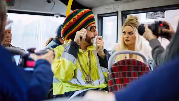 Ali G (Sacha Baron Cohen) adjusts his sunglasses on a bus beside a blonde woman
