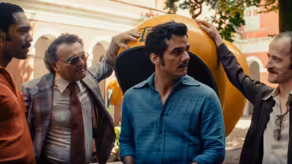 Four men gather around large yellow structure outdoors near columned building