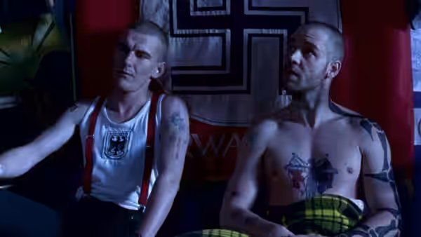 Hando (Russell Crowe) sits shirtless beside another man before a large flag