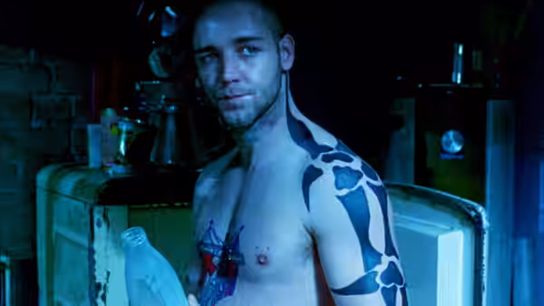 Hando (Russell Crowe) holds a bottle while standing shirtless in a dim kitchen