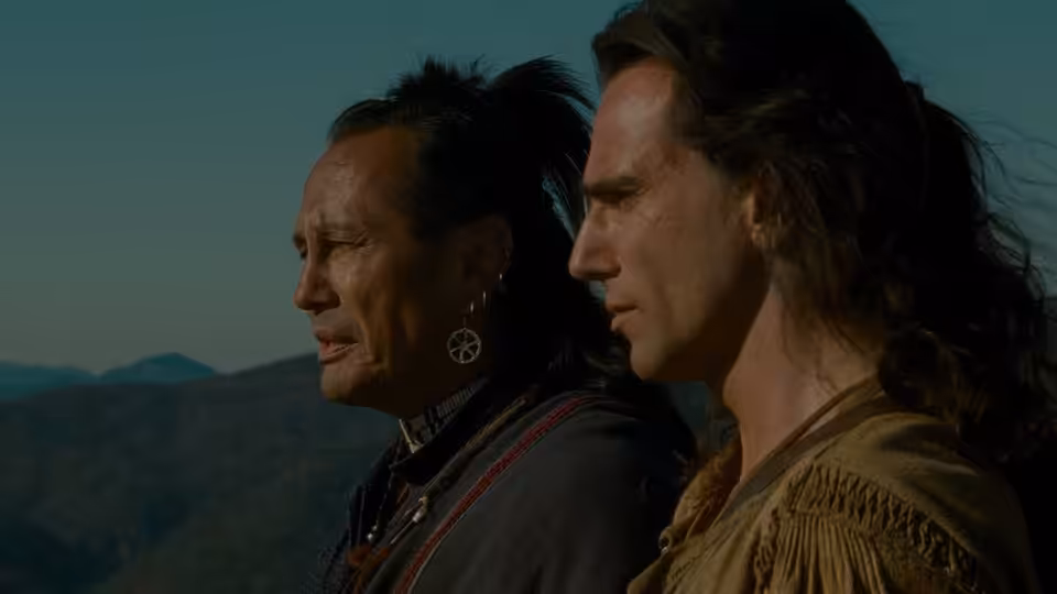 Chingachgook (Russell Means) and Hawkeye (Daniel Day-Lewis) standing in profile against mountain landscape