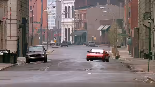Two cars driving on an empty city street lined with buildings