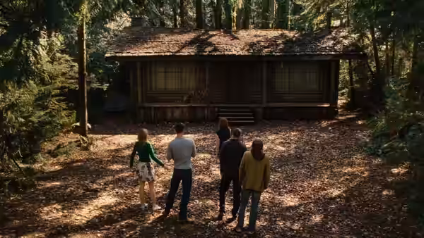 Five young people approaching a wooden cabin in the forest