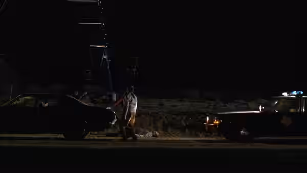 A man stands by a car at night beside a police cruiser