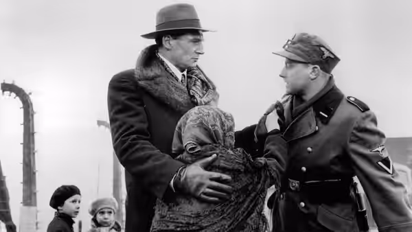 Man in fur collar coat speaking to an officer while holding an elderly woman