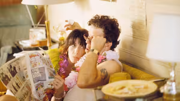 Couple wearing leis on a couch with the woman holding a newspaper