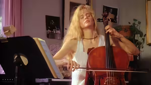 Blonde woman playing cello with eyes closed in a sunlit room