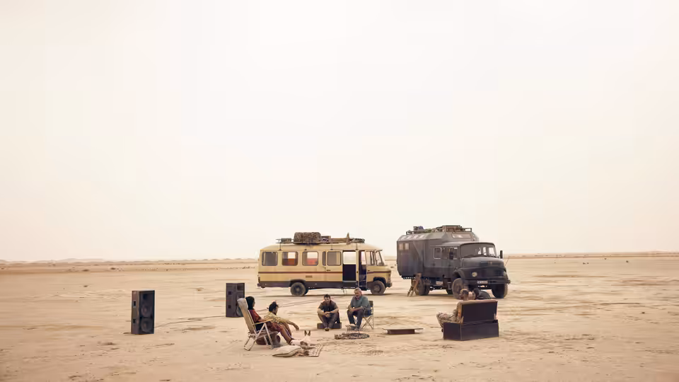 people sitting in chairs beside two vehicles in a desert