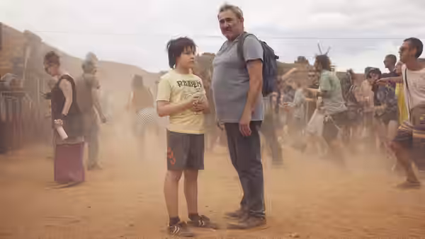 Luis (Sergi López) standing with Esteban (Bruno Núñez) in a dusty crowd