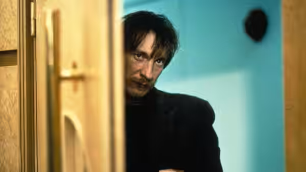 Johnny (David Thewlis) peering through open doorway into room