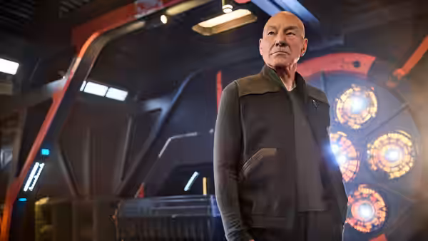 Jean-Luc Picard (Patrick Stewart) stands aboard a starship beside glowing circular consoles