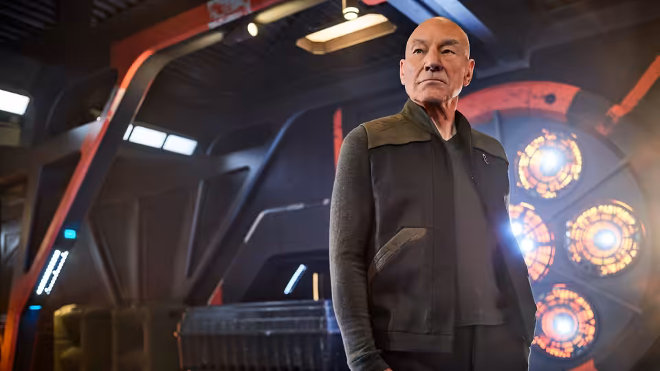 Jean-Luc Picard (Patrick Stewart) stands aboard a starship beside glowing circular consoles
