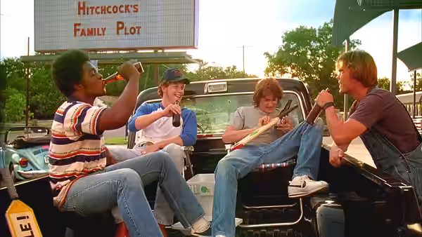 Four young men sitting in a pickup truck bed drinking and holding a paddle