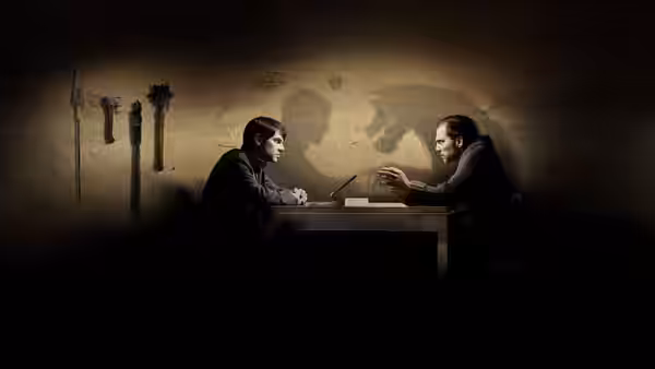 Two men sit across a table as one gestures toward the other