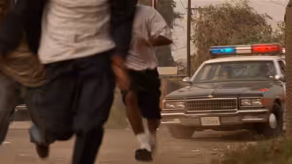 Several young men run down a street away from a police car