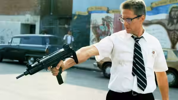 D-Fens (Michael Douglas) extending submachine gun across empty street