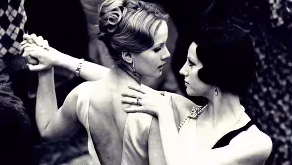 Two women in evening gowns dance closely together in black and white