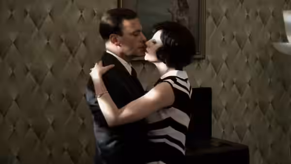 A man in a suit embraces a woman in a striped dress indoors