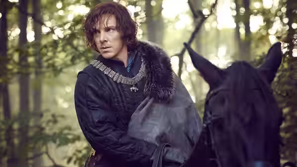 A man in a fur-trimmed coat sits on horseback in the woods