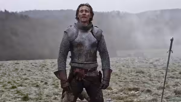 An armored man stands in a misty field beside a planted sword