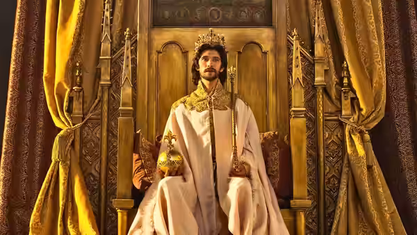 King Richard (Ben Whishaw) sits crowned between golden curtains