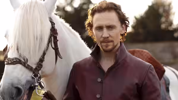 A man in a burgundy coat stands beside a white horse