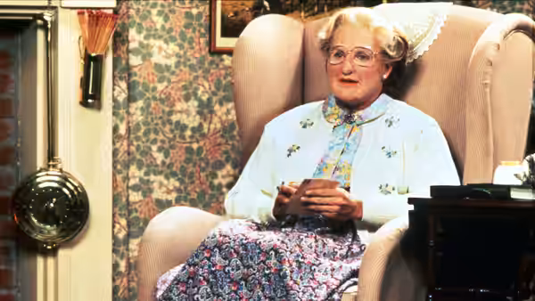 Mrs. Doubtfire (Robin Williams) seated in an armchair holding a cup