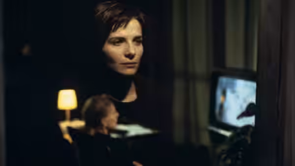 Julie (Juliette Binoche) standing in a dark room beside a television