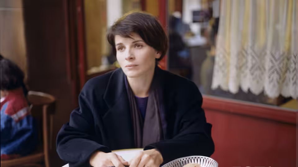 Julie (Juliette Binoche) seated at a table indoors with hands clasped