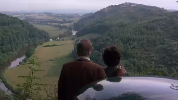 a couple standing beside a car overlooking a river valley