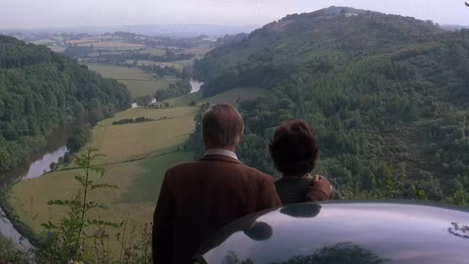 a couple standing beside a car overlooking a river valley