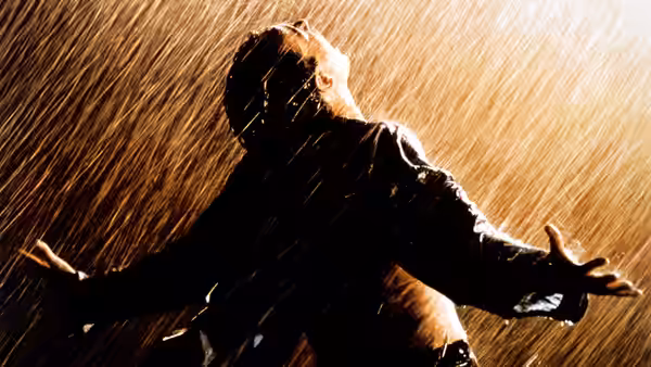a man stands in heavy rain with arms outstretched looking upward